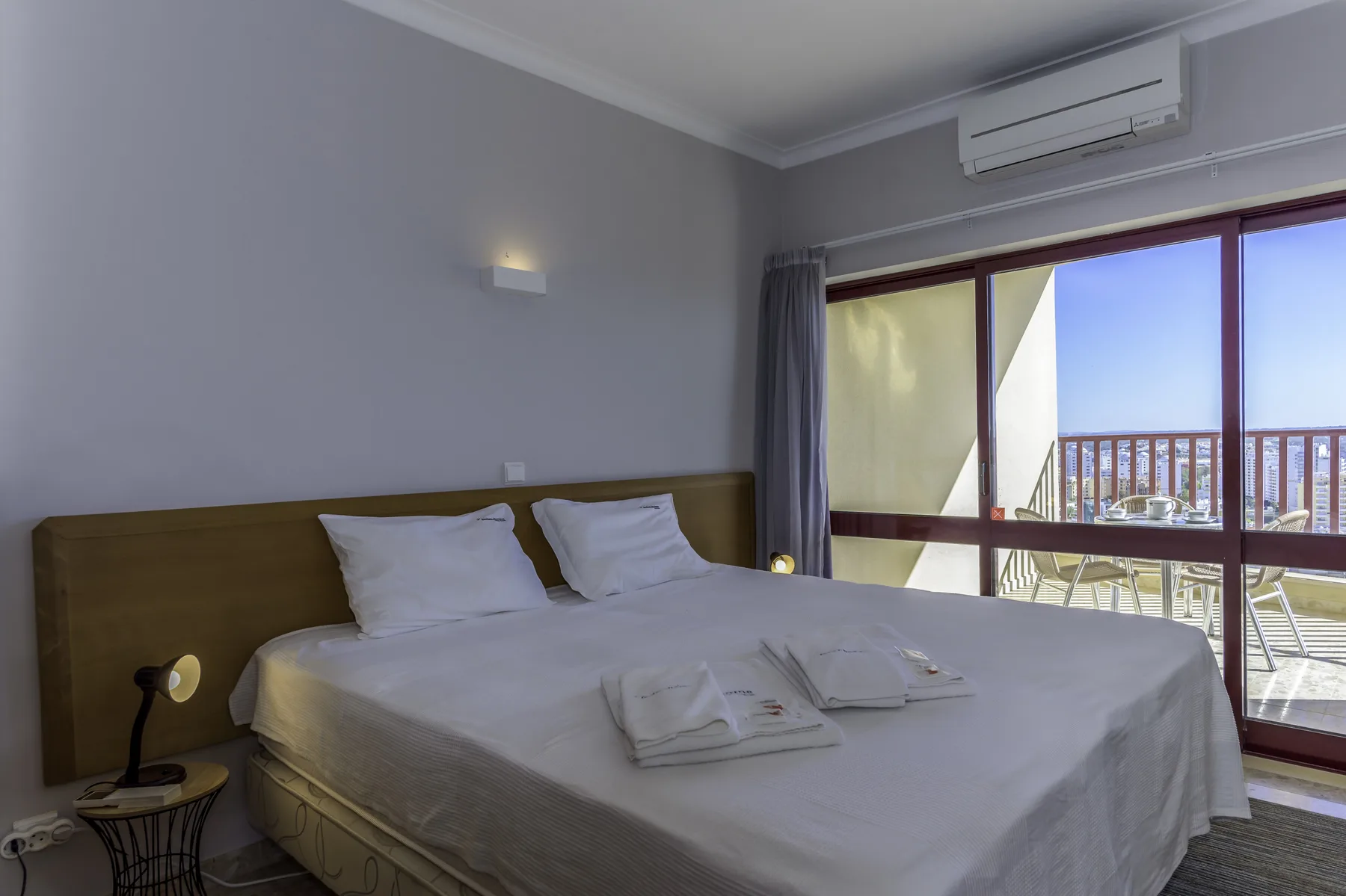 A bedroom with a neatly made bed beside sliding glass doors opening onto a balcony.