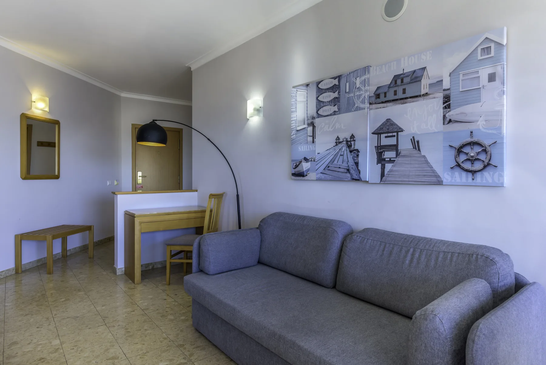 A living room with gray seating, a small dining table, and coastal wall art.