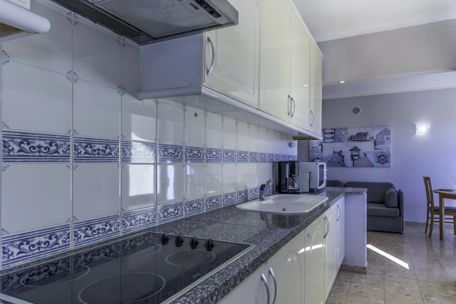 A tiled kitchen with a countertop and a living area visible beyond it.