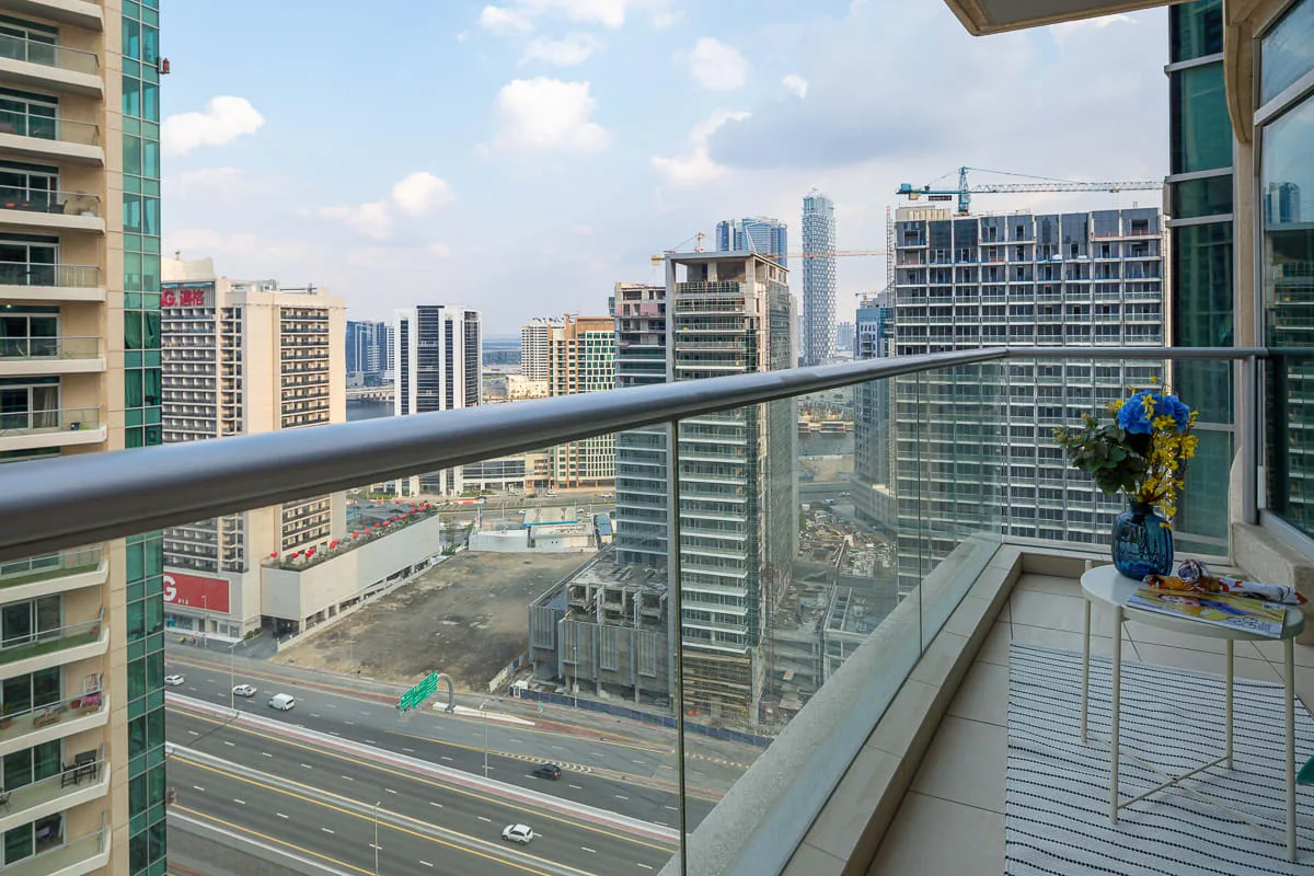 A balcony overlooks nearby high-rise buildings and a busy road.