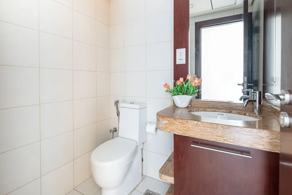 A tiled bathroom with a toilet and a sink beside a bright window.