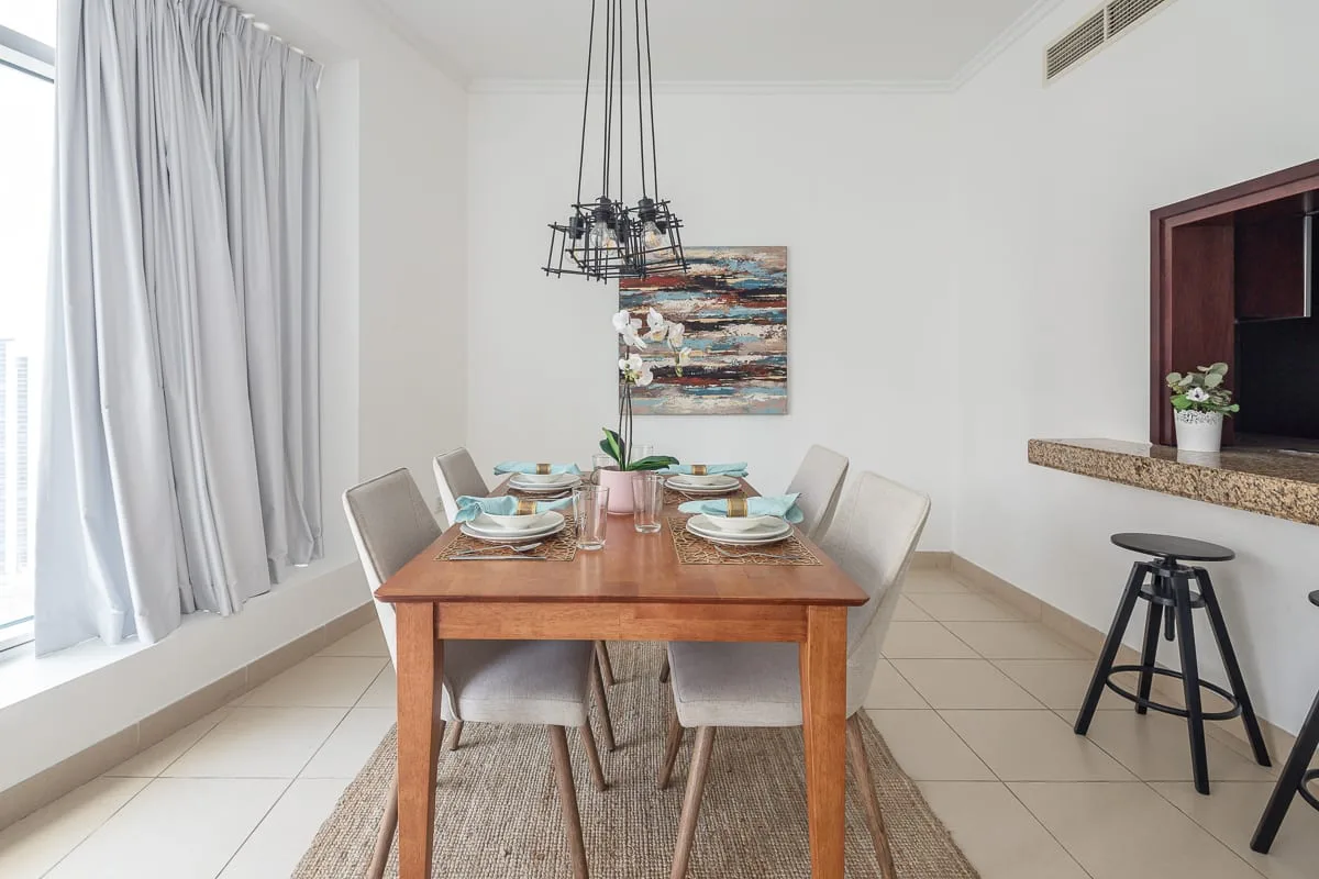 A bright dining area with a wooden table set beneath a hanging light.
