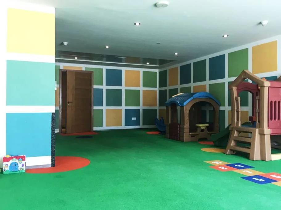 A colorful indoor play area has padded flooring and small play structures.