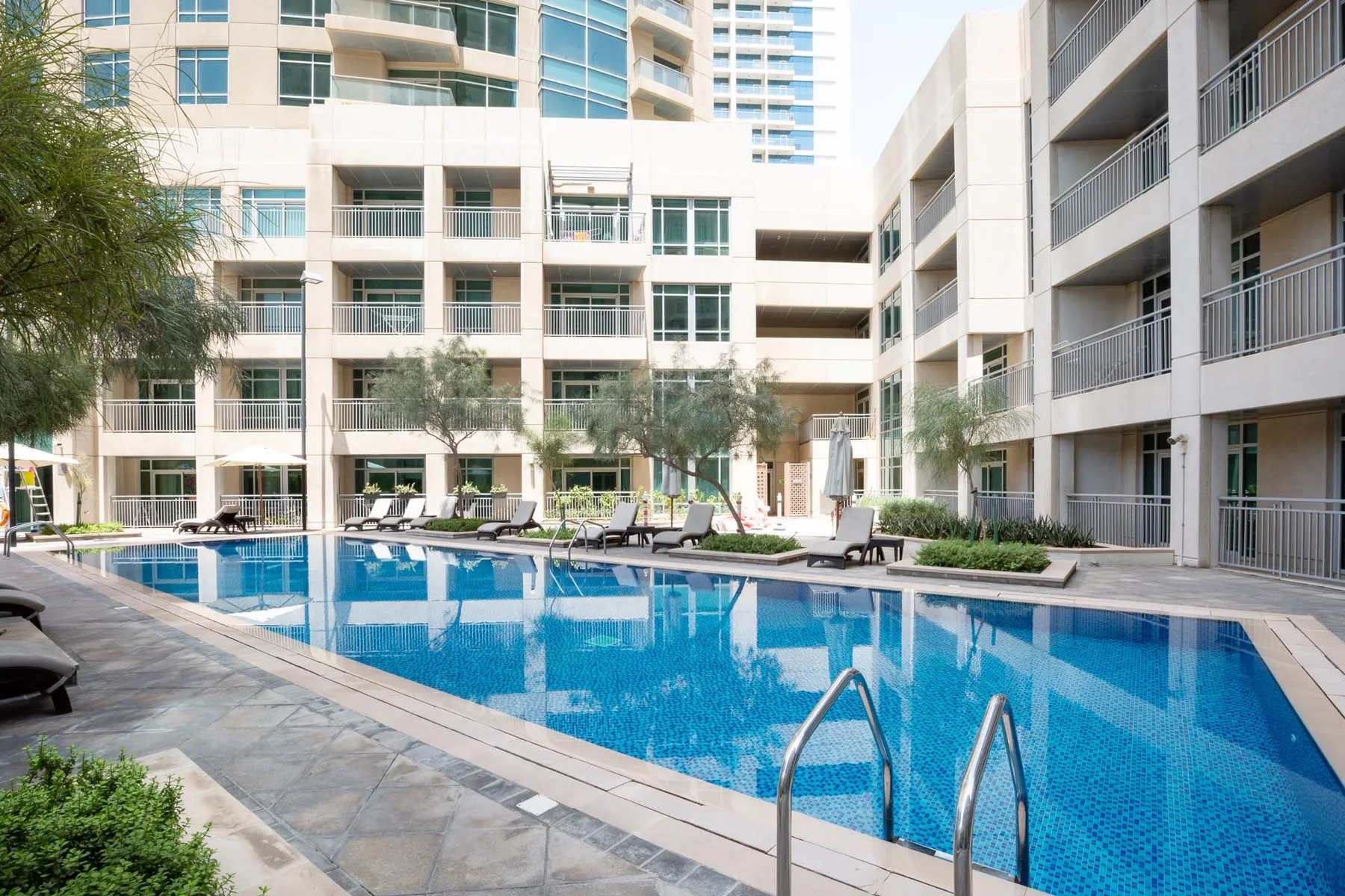 An outdoor swimming pool sits among modern multi-story buildings.