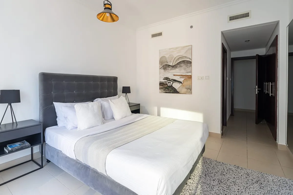 A bright bedroom with a neatly made bed and artwork on the wall.