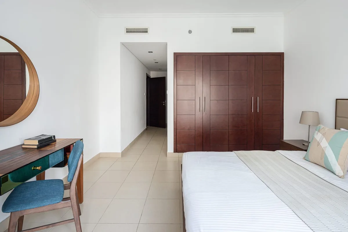 A bright bedroom with a large wooden wardrobe and a neatly made bed.