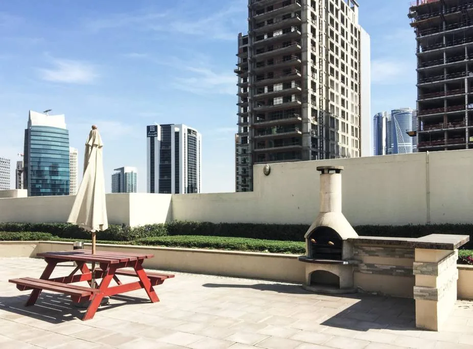A rooftop patio with picnic seating and a built-in outdoor fireplace, set against city buildings.