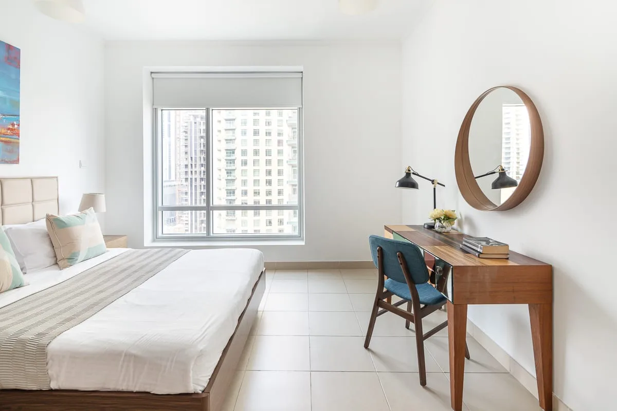 A bright bedroom with a bed and a wooden desk beside the window.