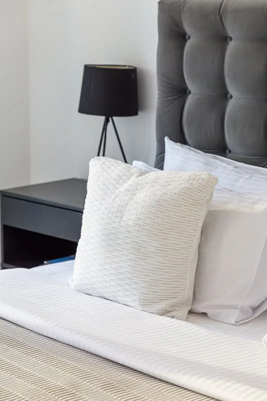 A bedroom with white bedding and a dark upholstered headboard.