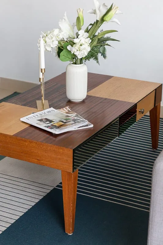 A wooden coffee table displays a vase of flowers and a magazine in a living room.