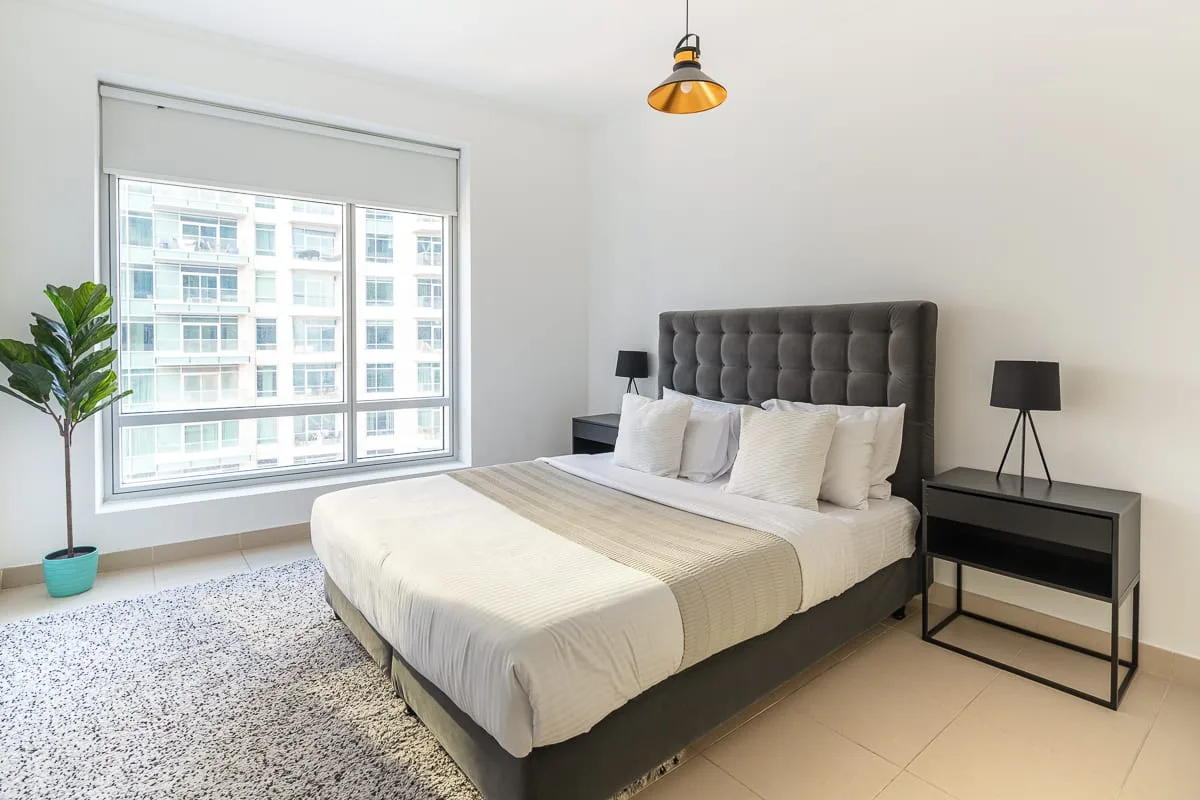 A bright bedroom with a large bed beside a window and bedside tables.