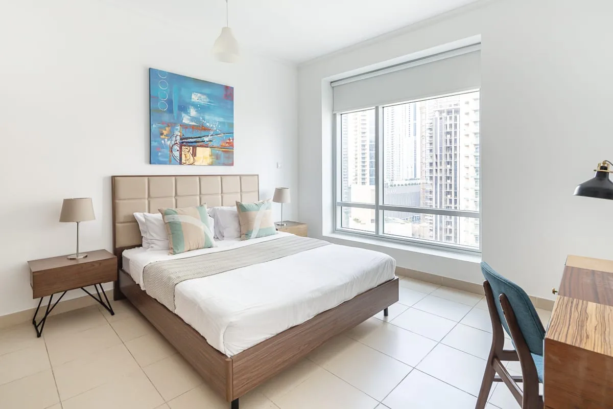 A bright bedroom with a neatly made bed and a large window.