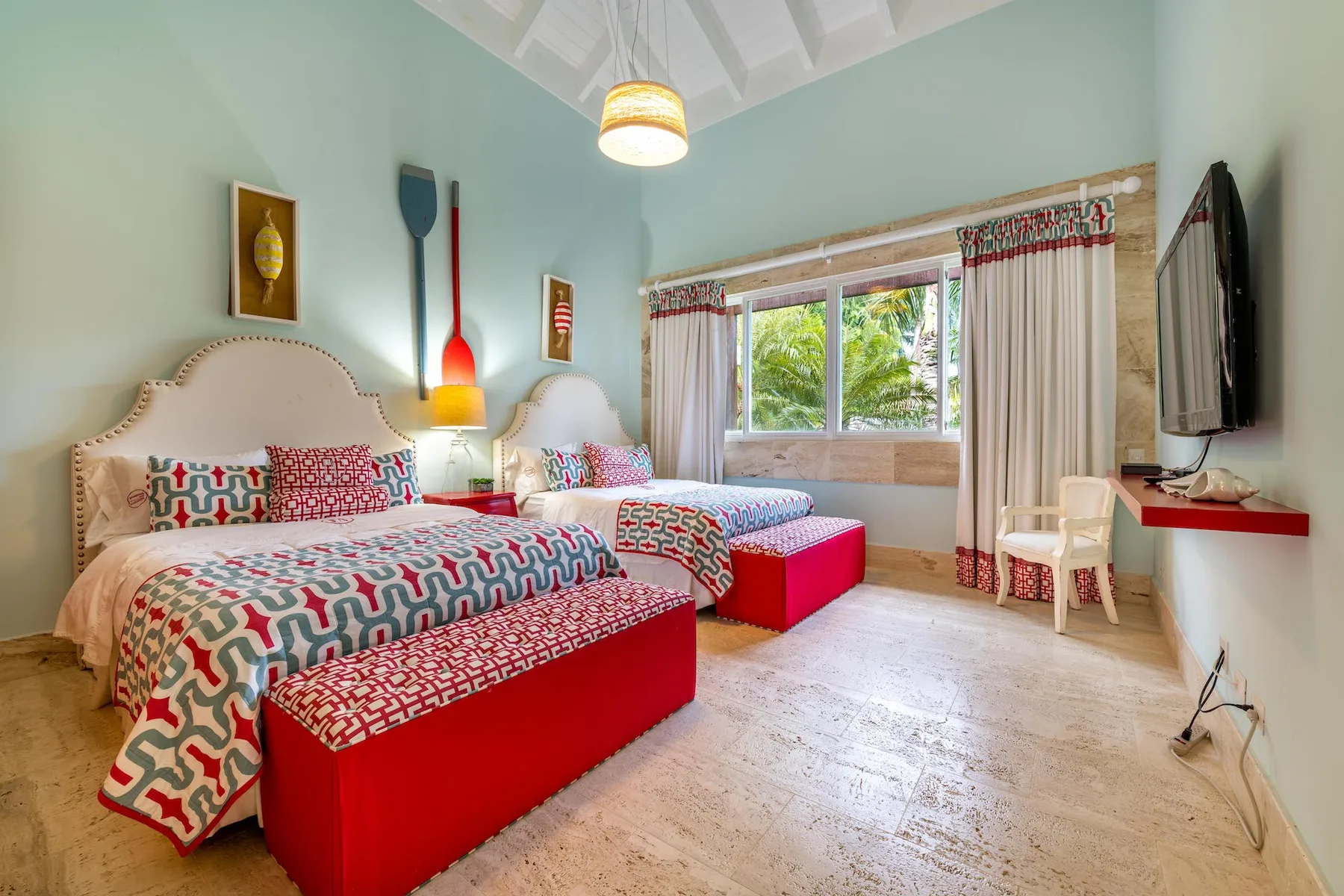A bright bedroom with two beds, colorful patterned bedding, and a large window.