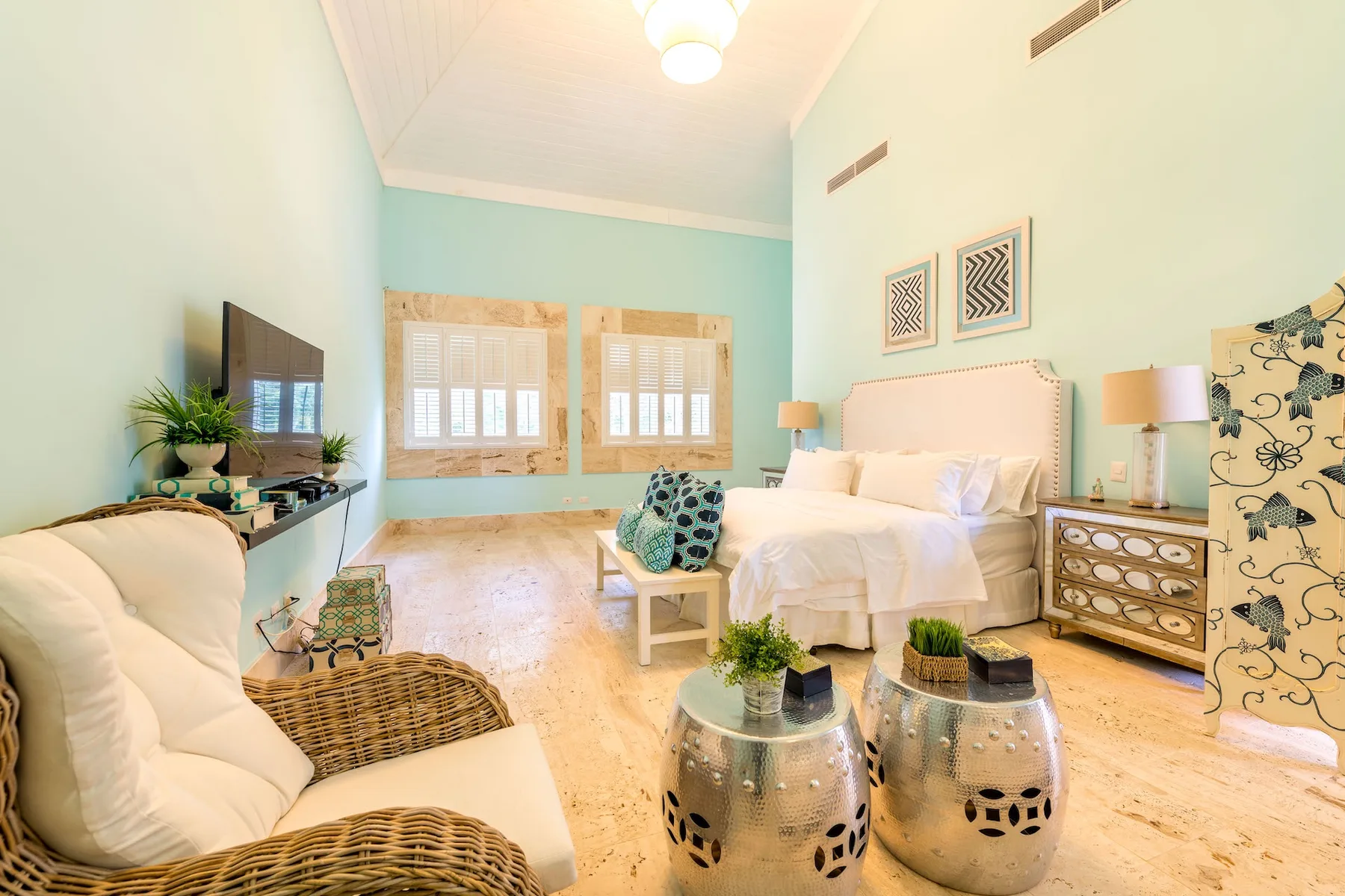 Un dormitorio luminoso con una cama, asientos y ventanas con vistas al jardín.