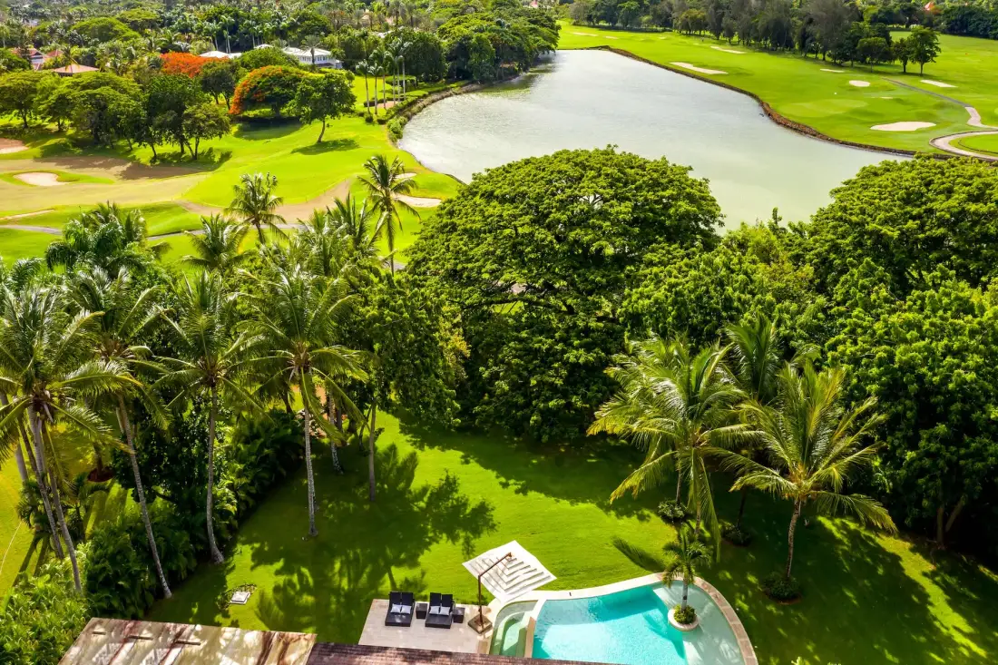 Aerial view of a tropical garden with a pool and a lake beyond.
