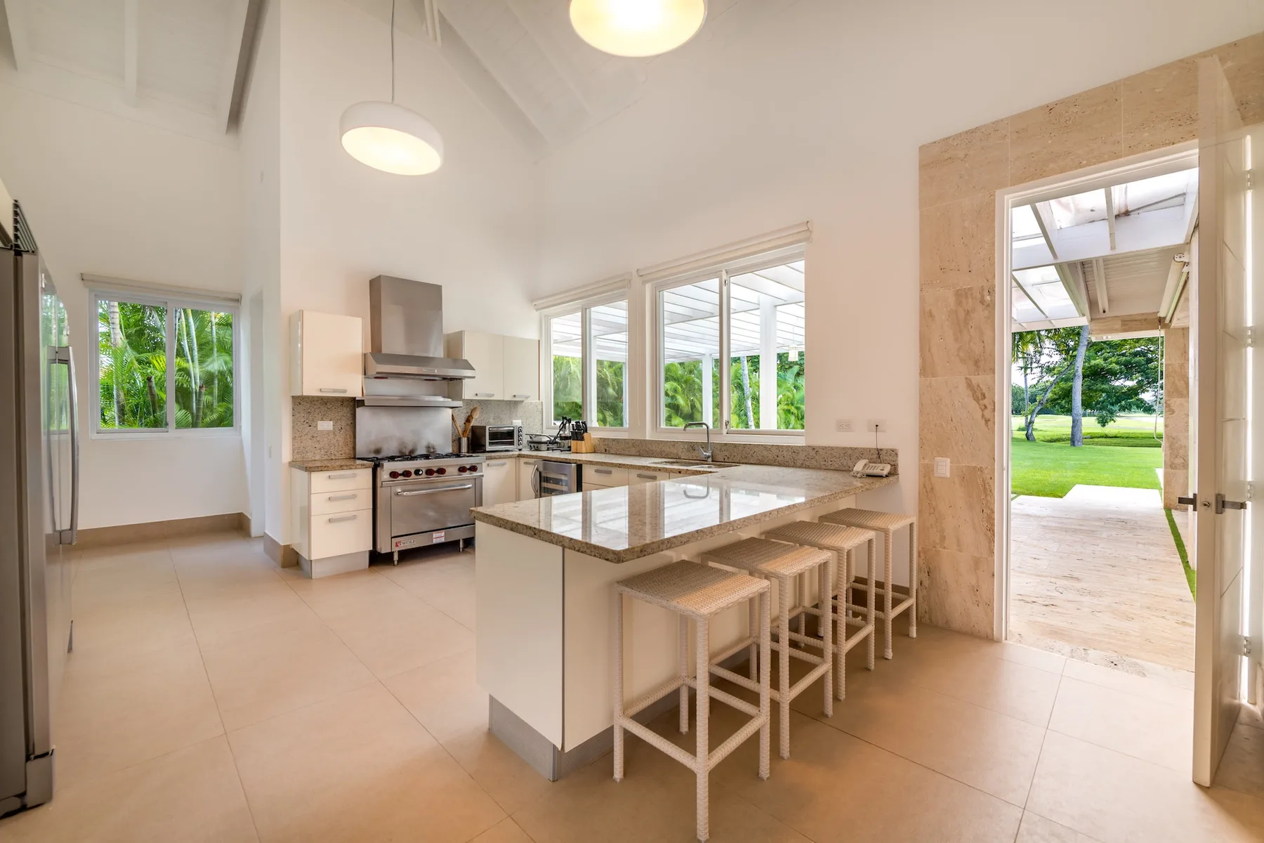A bright kitchen with a central island, stools, and large windows.