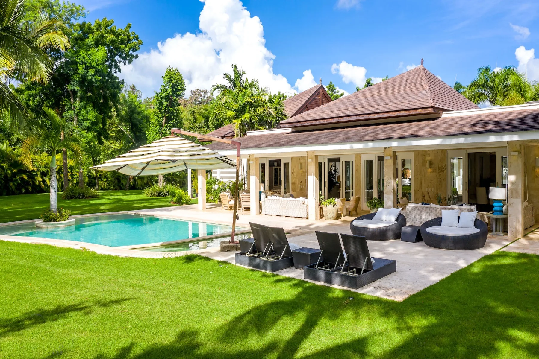 Patio de una villa tropical con asientos al aire libre junto a una piscina y césped verde.
