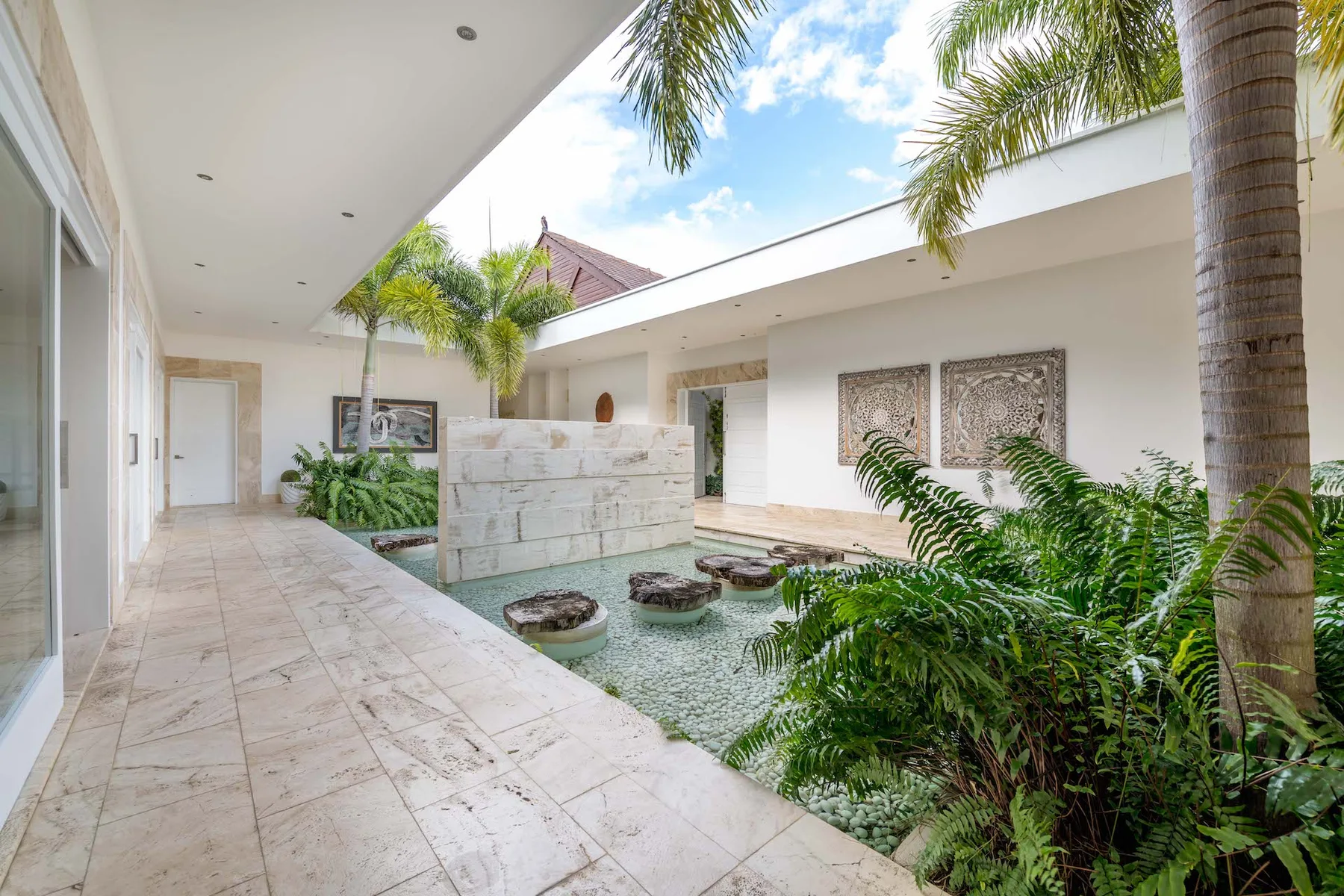 A bright courtyard with a shallow water feature, tropical plants, and a tiled walkway.