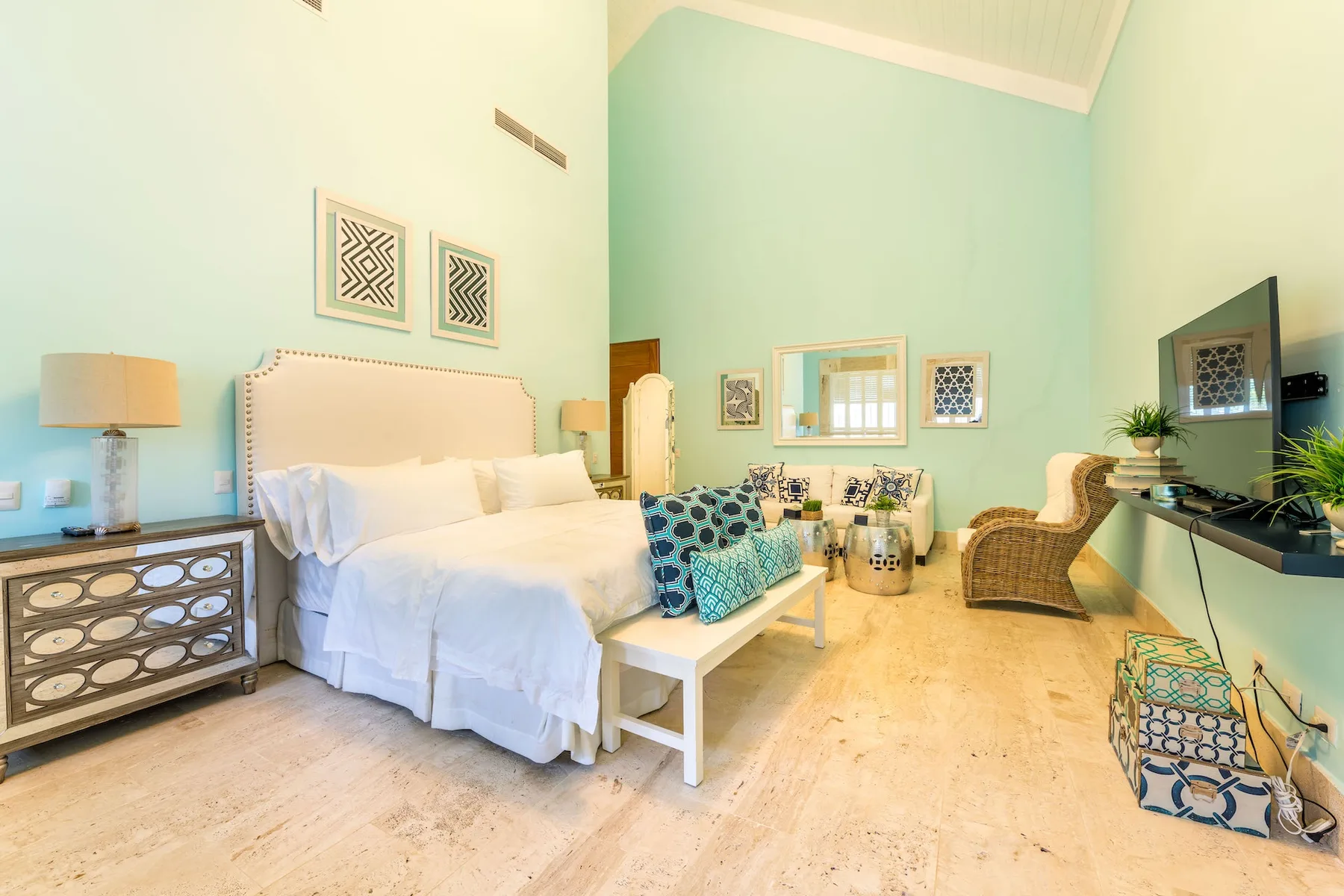 Un dormitorio luminoso con una cama blanca, asientos y un televisor.