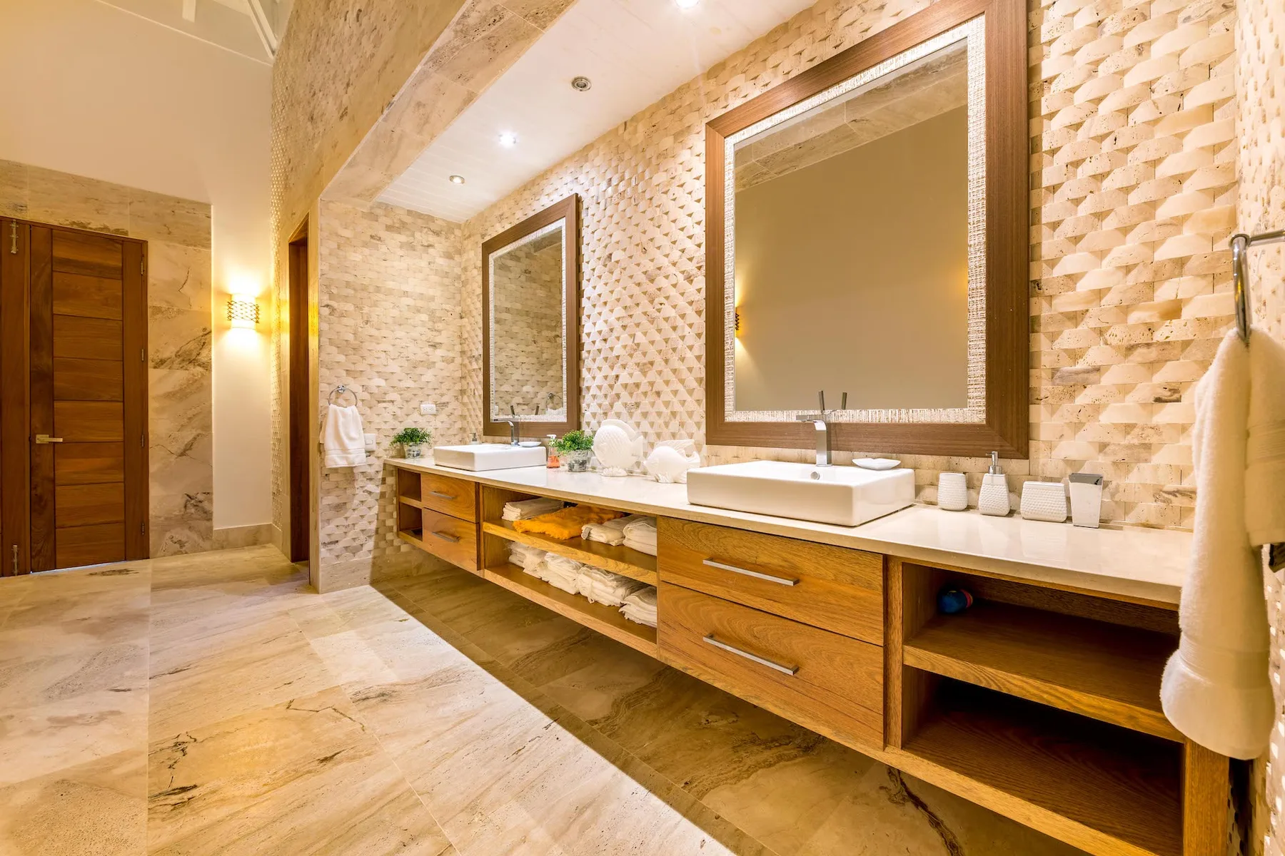Un baño amplio cuenta con un largo tocador de madera, lavabos sobre la encimera y espejos grandes.