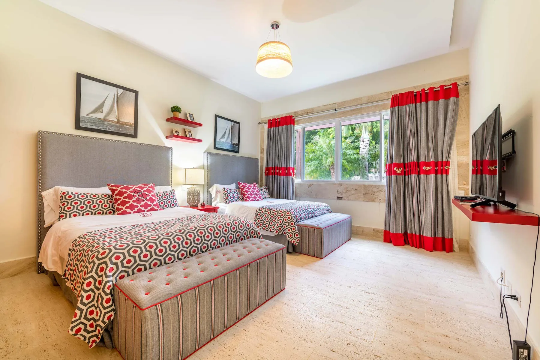A bedroom with patterned bedding, a window, and red-and-gray curtains.