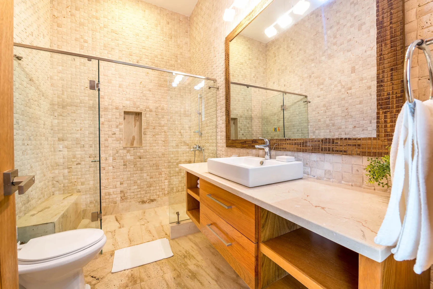 A tiled bathroom with a glass shower, sink, and long vanity.