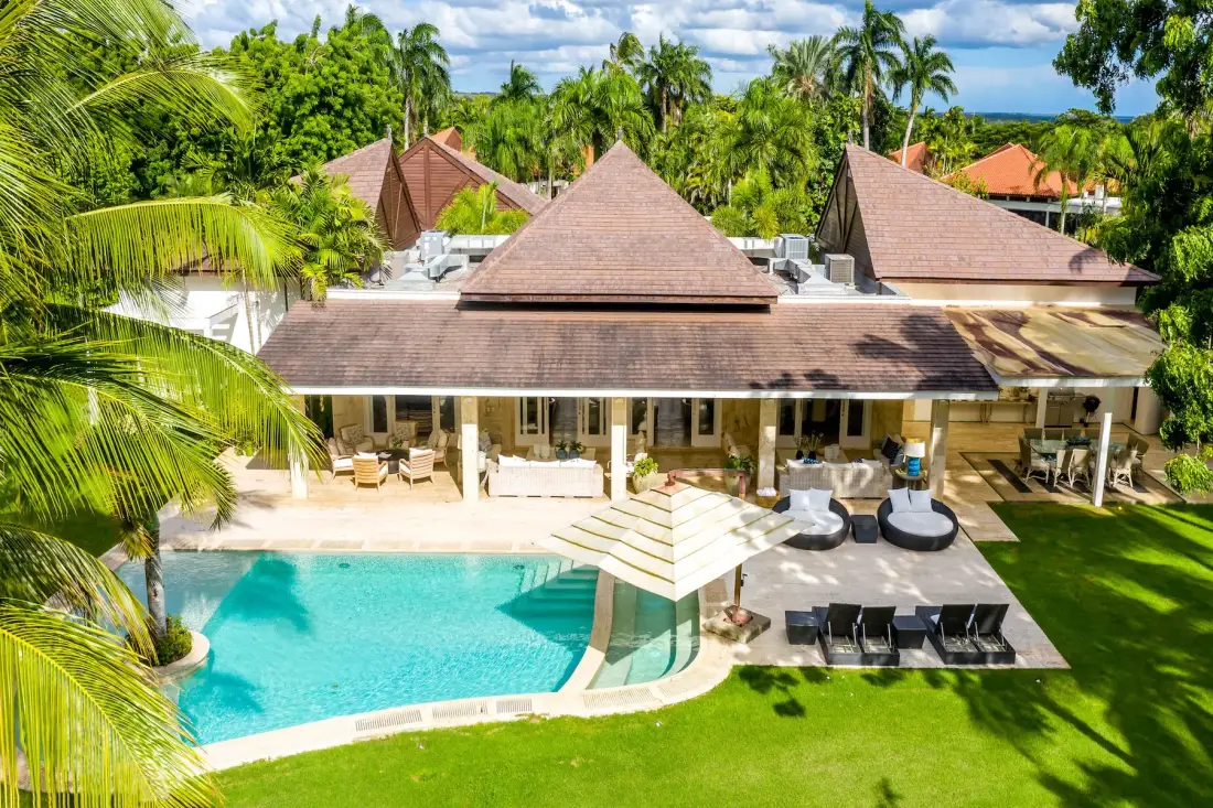 A tropical resort-style building overlooks a swimming pool and outdoor seating.