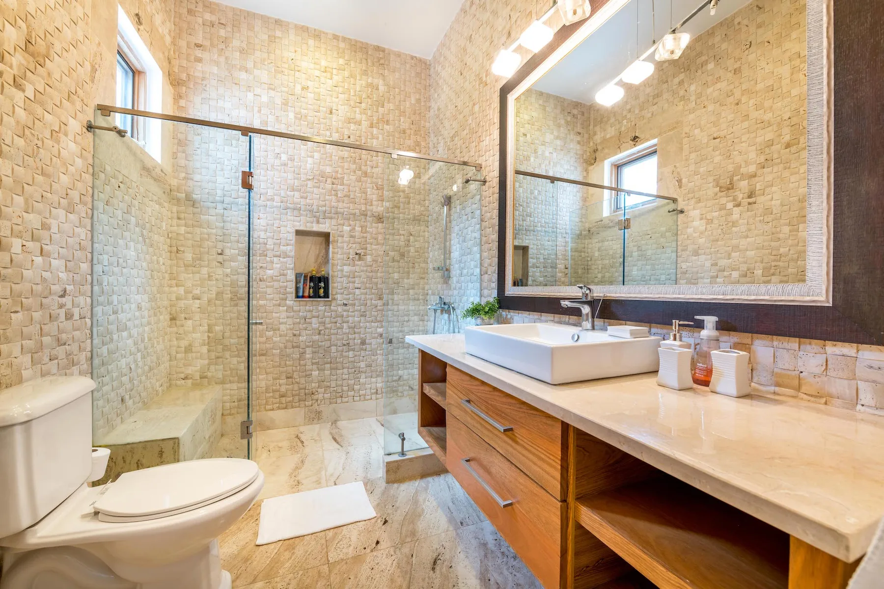 Un baño alicatado con ducha de vidrio, inodoro y tocador de madera.