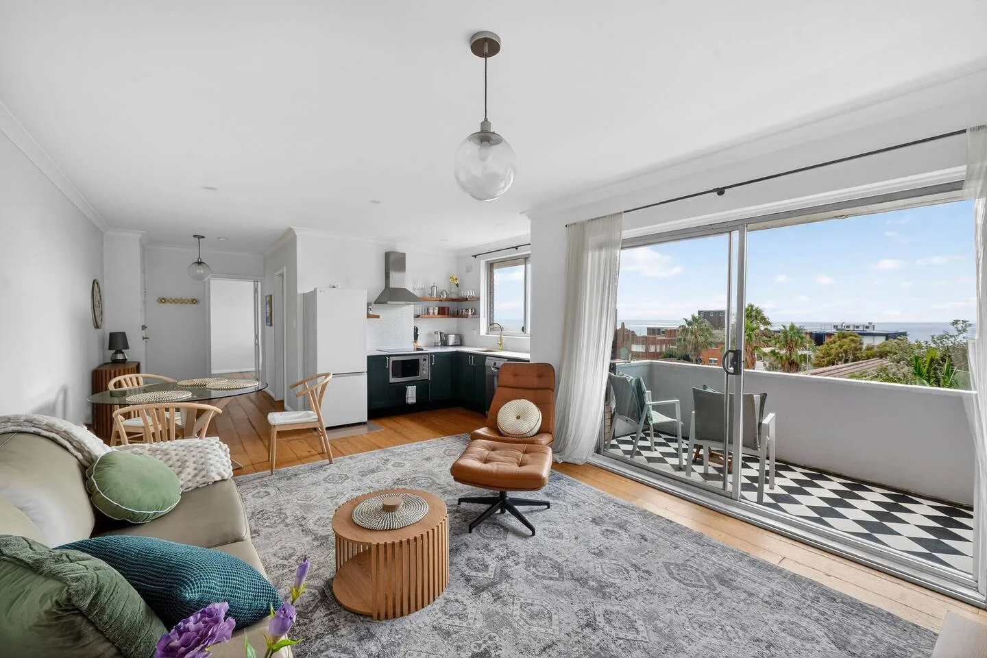 A bright living and dining area opens onto a balcony with distant ocean views.