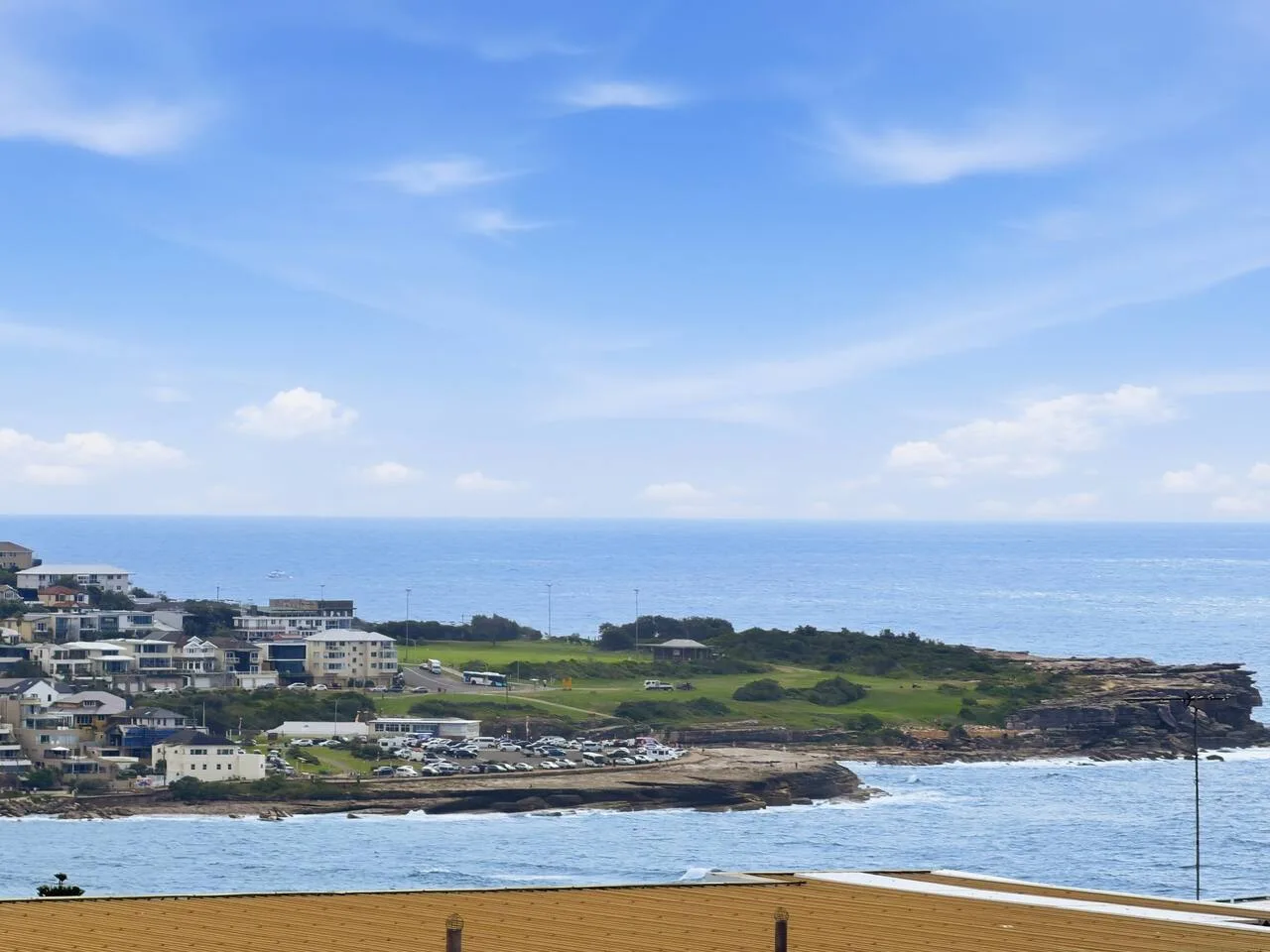 Coastal town and green headland beside the ocean under a blue sky.