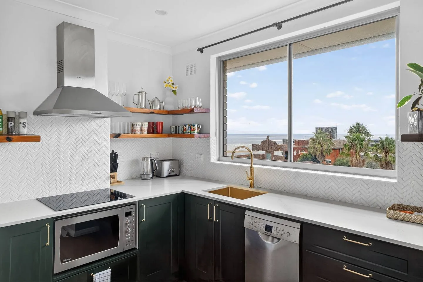 Prepare breakfast by the window as treetops and sea glimpses frame the kitchen in soft coastal light.