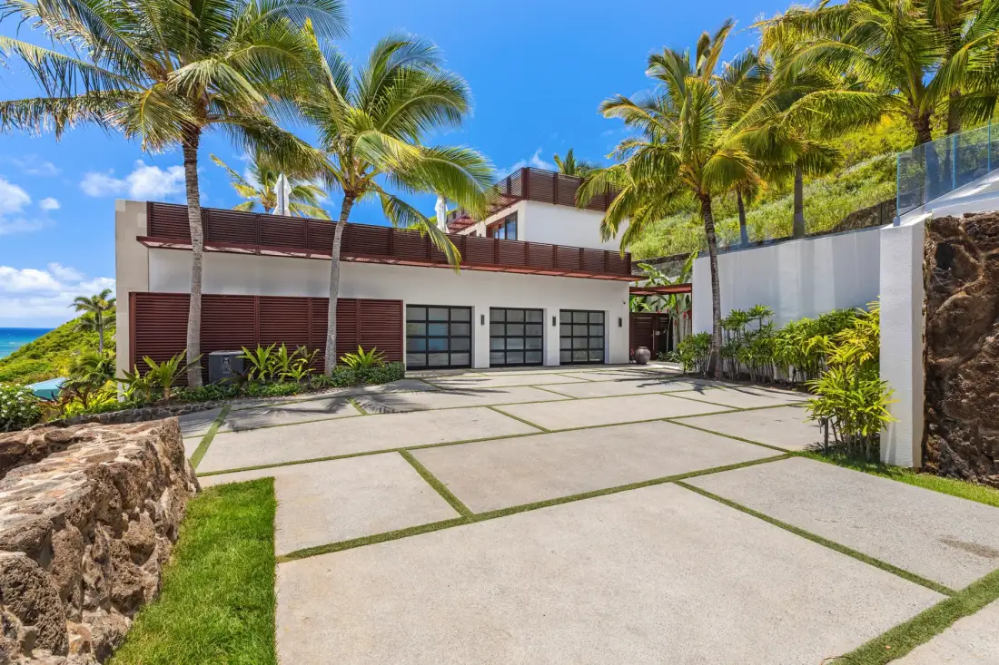 A modern building faces a paved driveway, with palm trees around it.