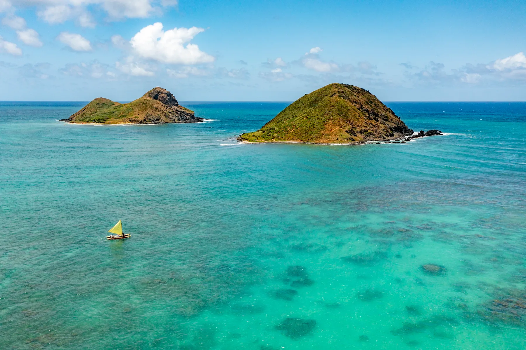 A turquoise sea surrounds two small green islands beneath a partly cloudy sky.