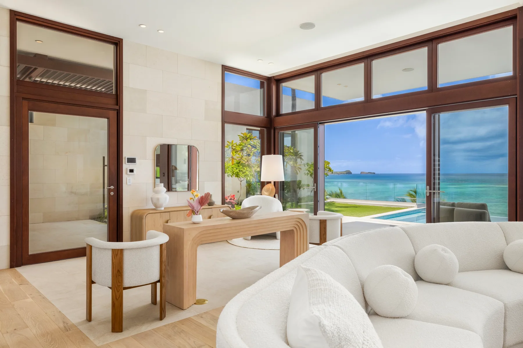 A bright living room with white seating and large windows overlooking the ocean.