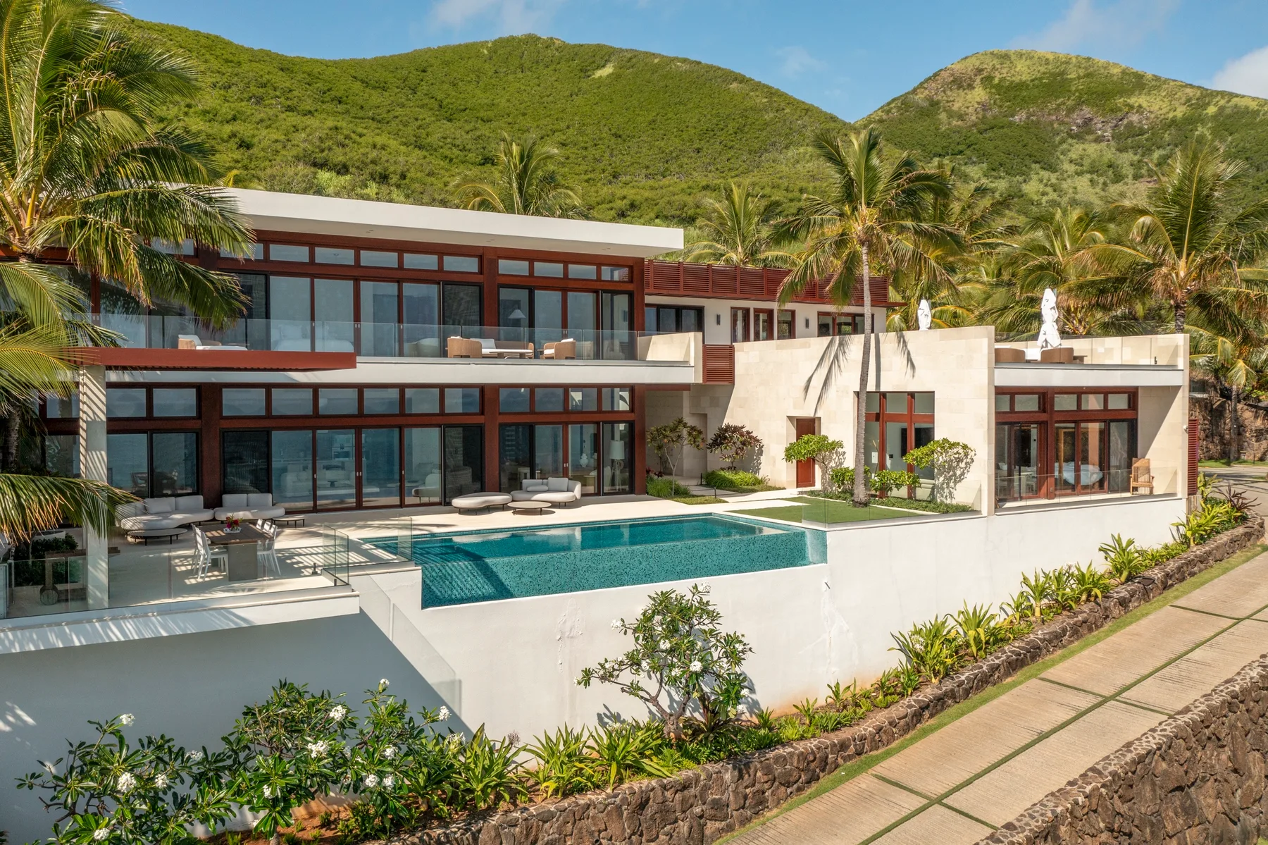 A modern villa overlooks a swimming pool, with green hills behind it.