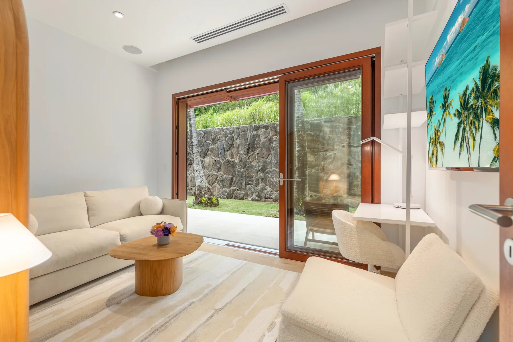 A bright living area with seating, a coffee table, and glass doors opening to greenery.