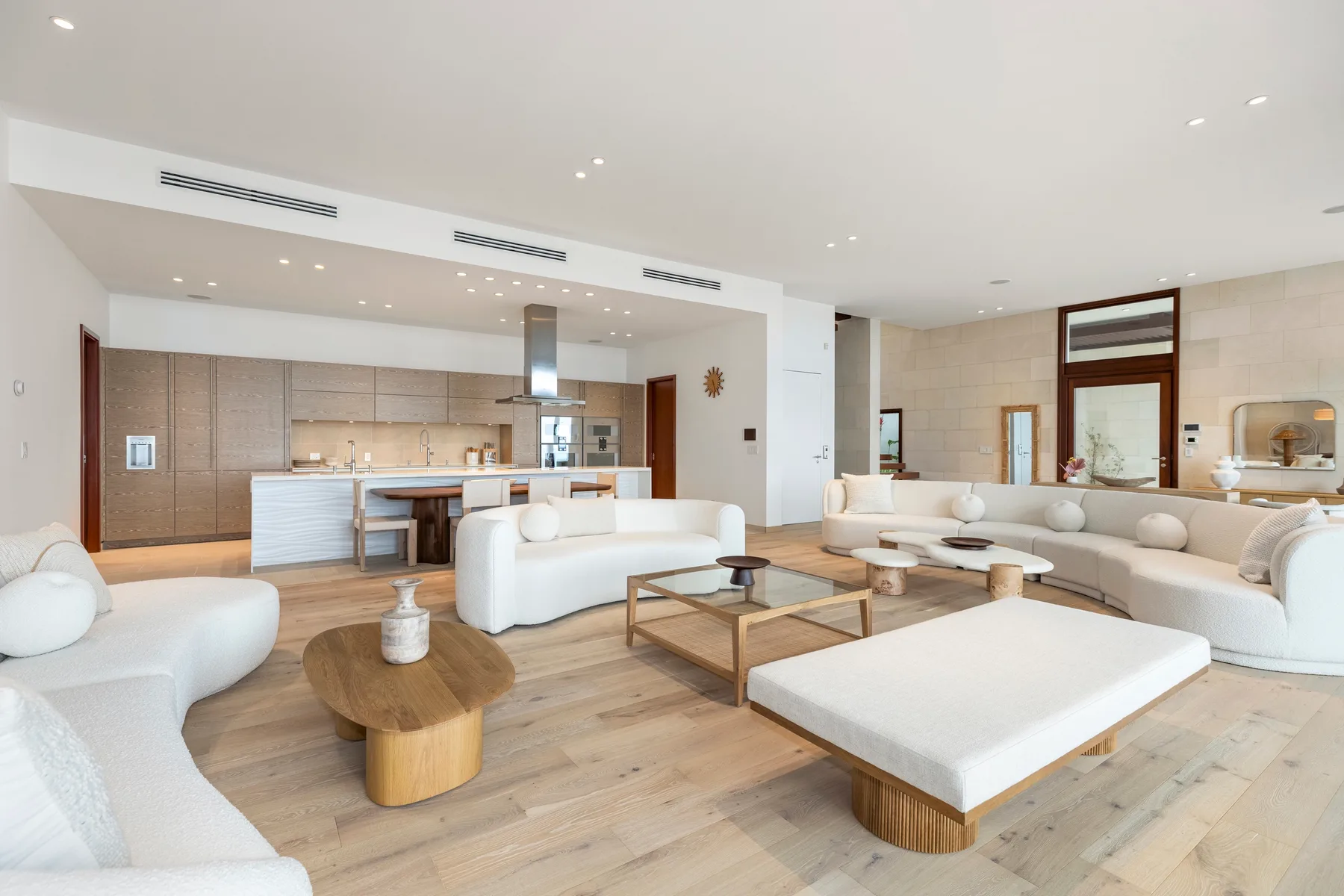 A bright open-plan living room with white seating and a kitchen in the background.