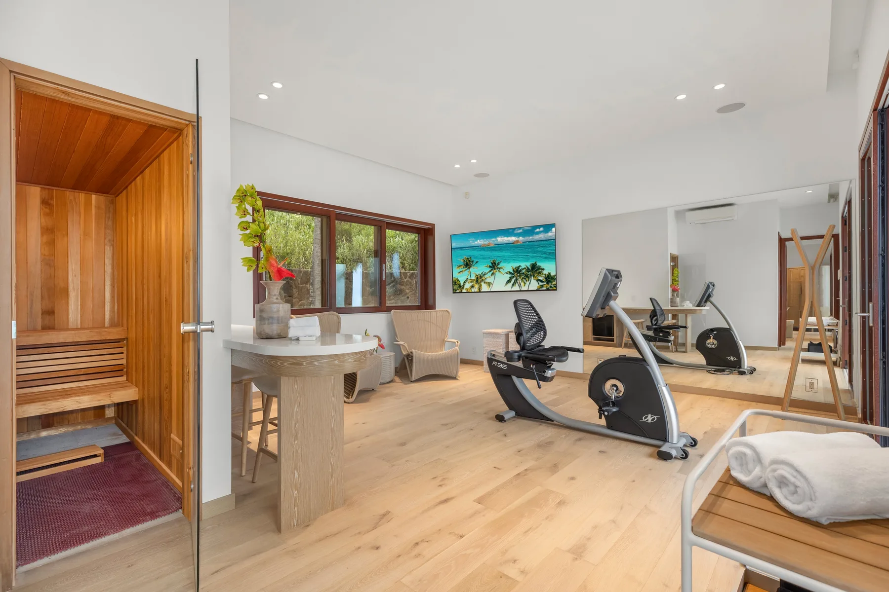 A bright fitness room with exercise equipment and a wooden sauna.