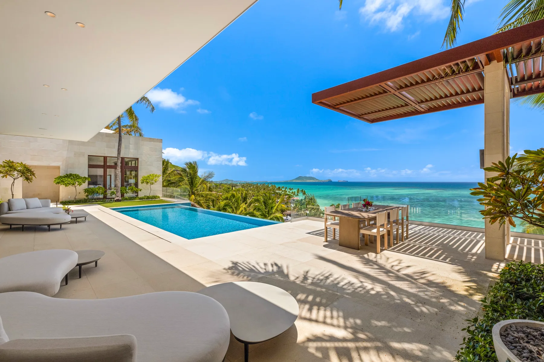 A seaside patio features a swimming pool, outdoor seating, and a dining table.