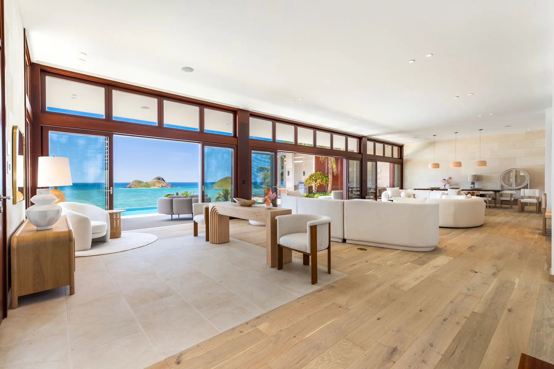 A bright open living room with seating beside large windows overlooking the ocean.