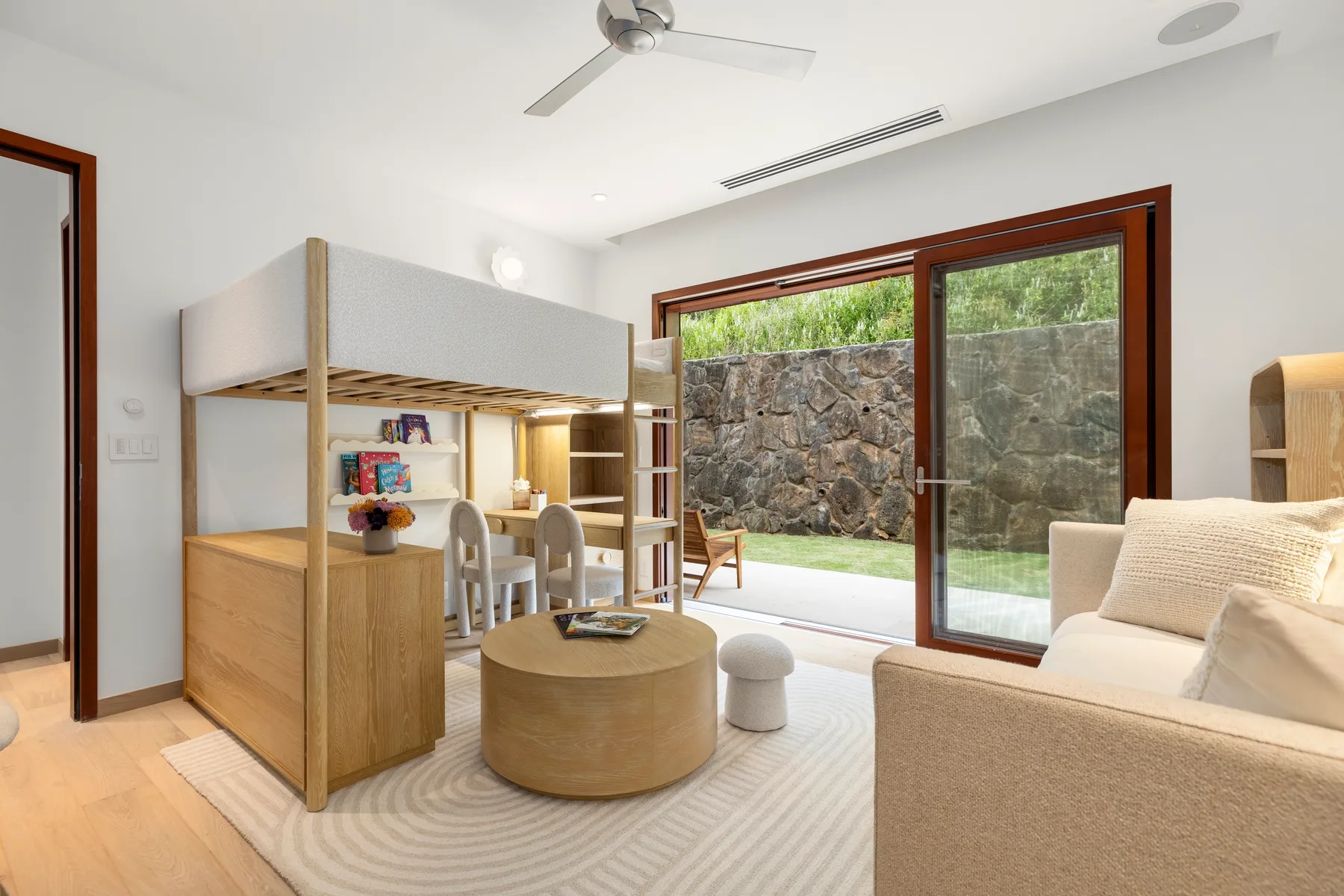 A bright bedroom has built-in bunk beds, a round table, and glass doors opening to a garden.