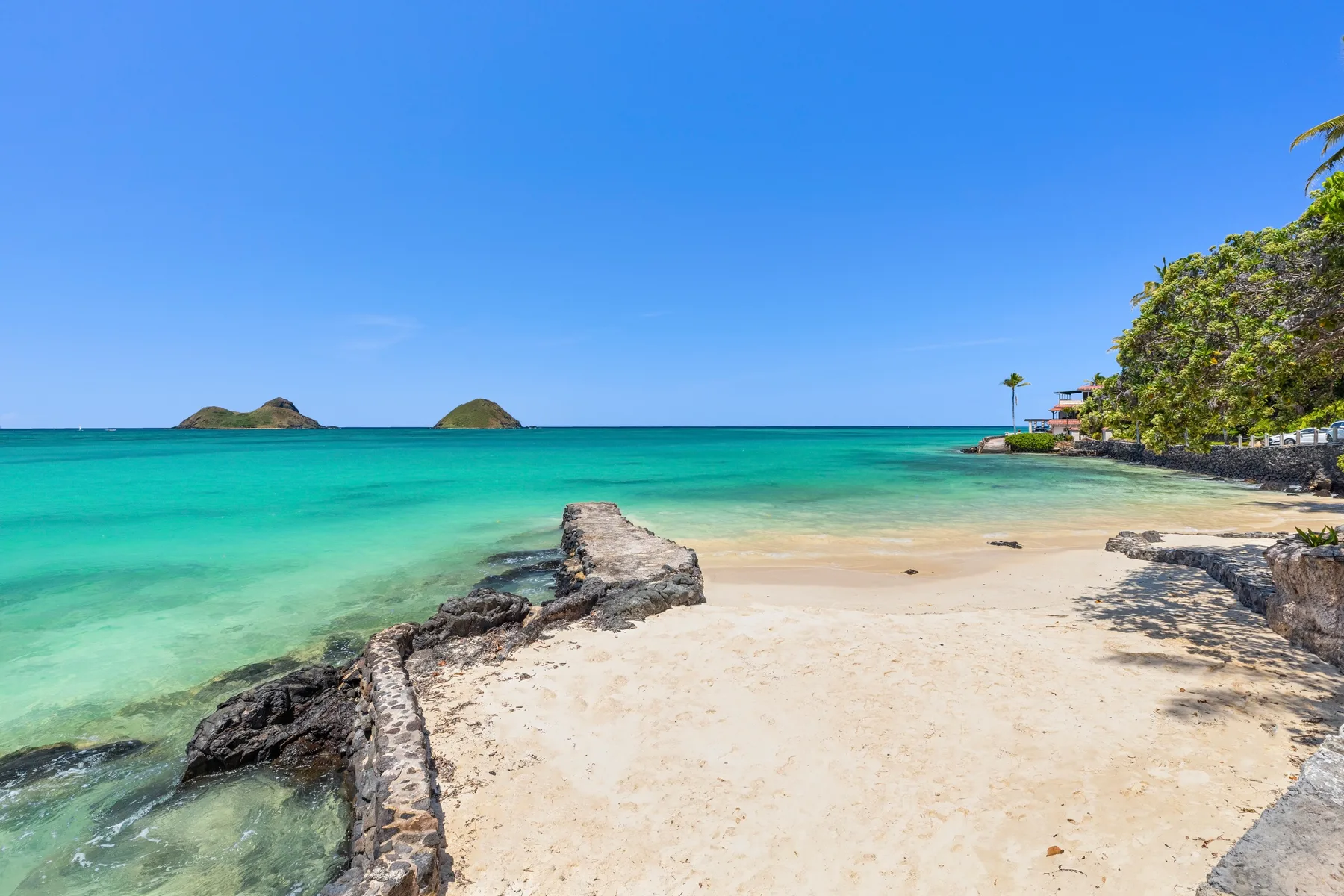 A sandy beach meets clear turquoise water beside a rocky shoreline.