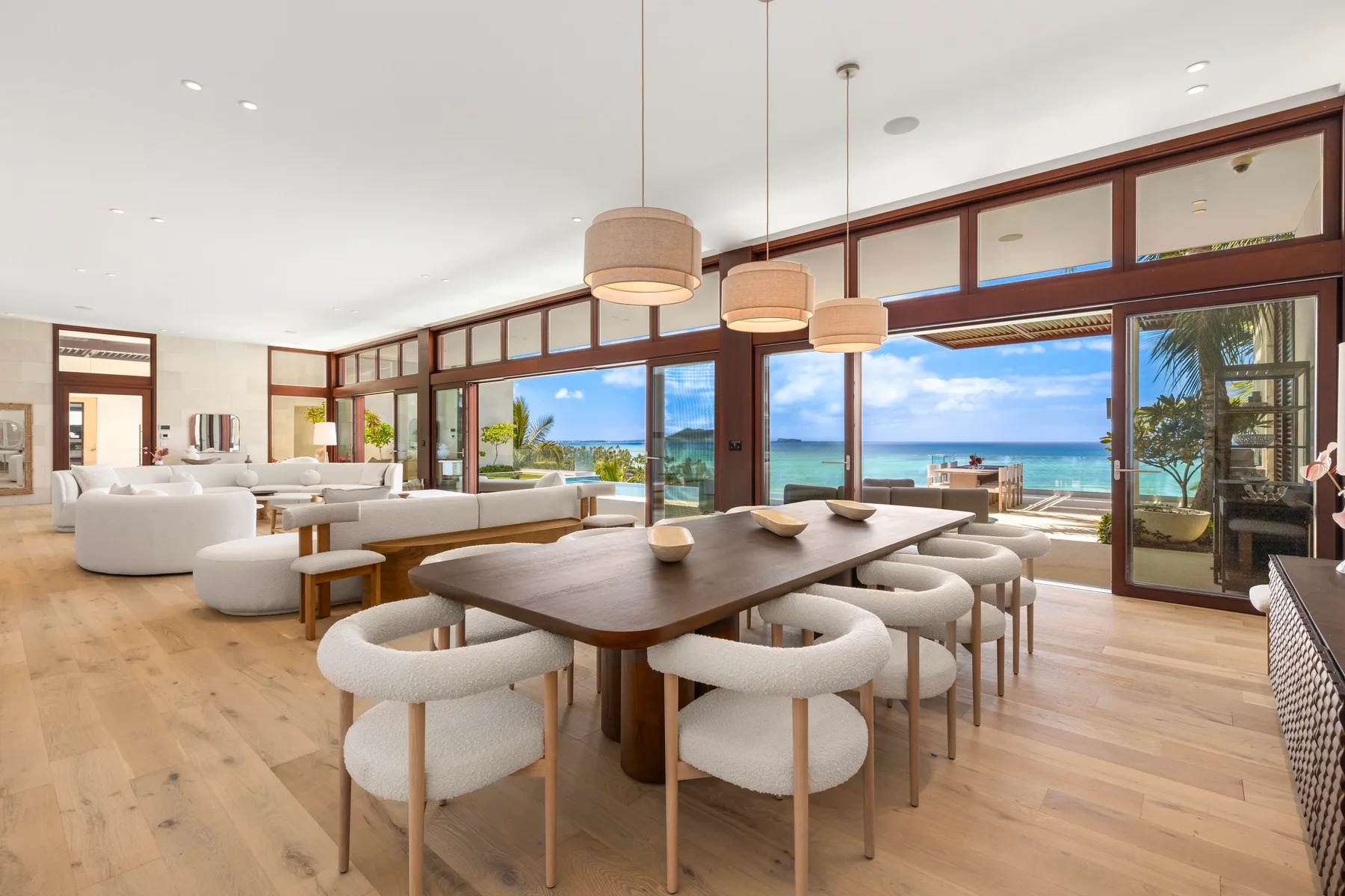 Una zona abierta de comedor y estar con una mesa grande frente a ventanas con vista al mar.