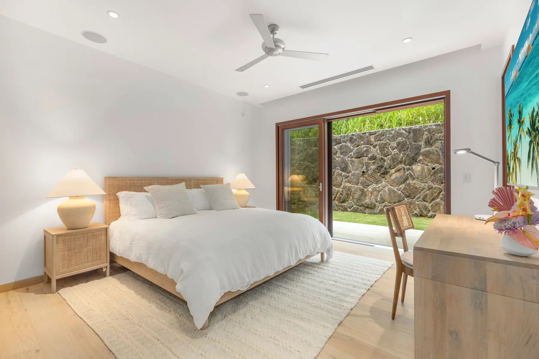 A bright bedroom with a bed, bedside tables, and a large glass door.