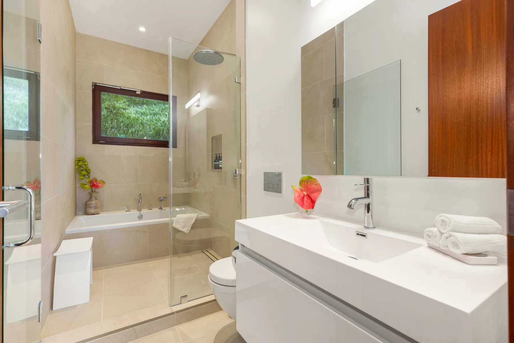 A bright bathroom with a bathtub, glass shower screen, and wide sink counter.