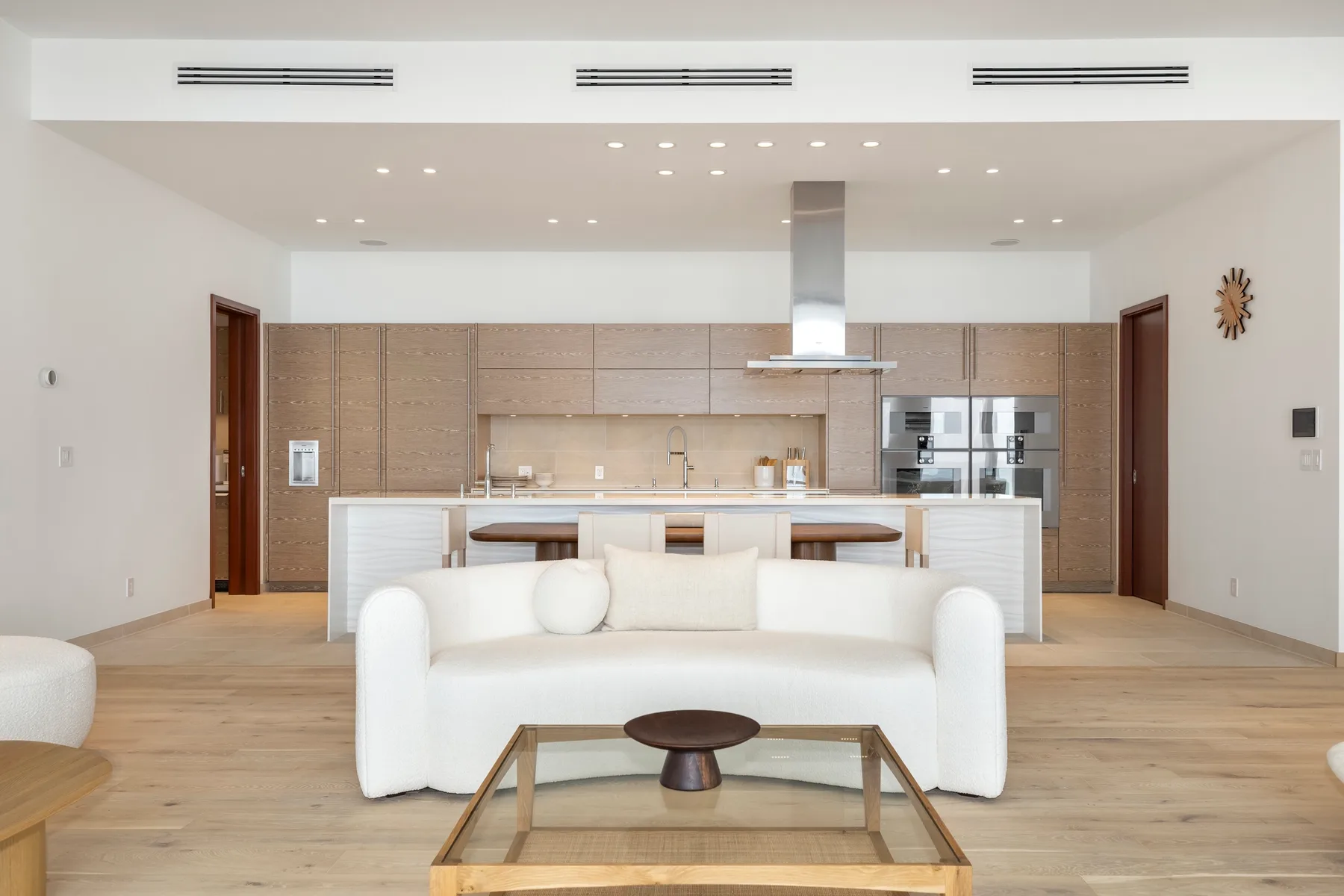 A bright living room with white seating facing an open kitchen.