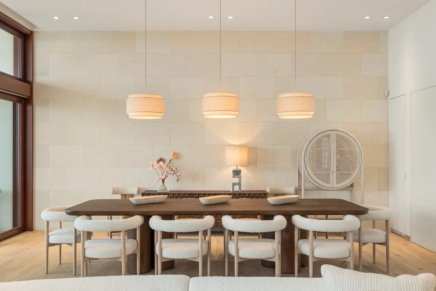 A dining area with a long table and cushioned seating beneath pendant lights.