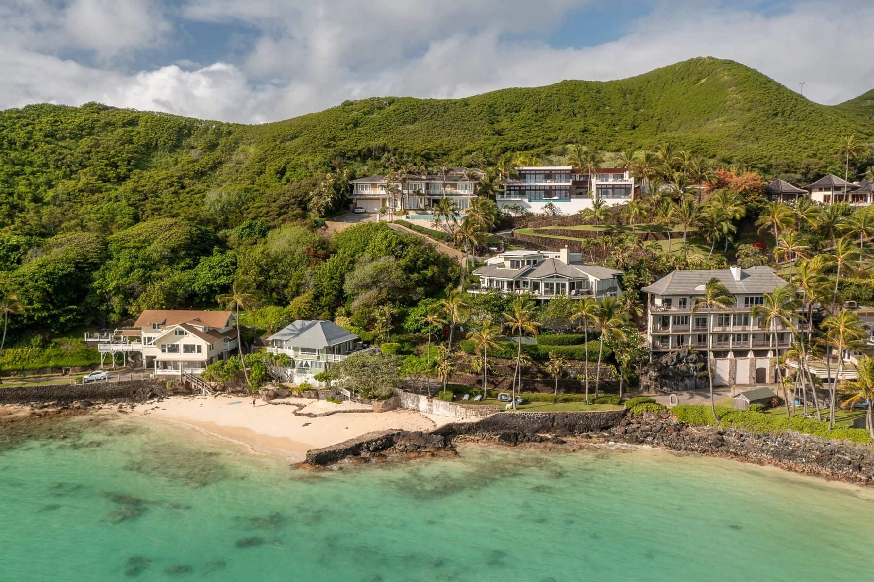 A coastal resort sits beside a sandy beach and turquoise water, backed by green hills.