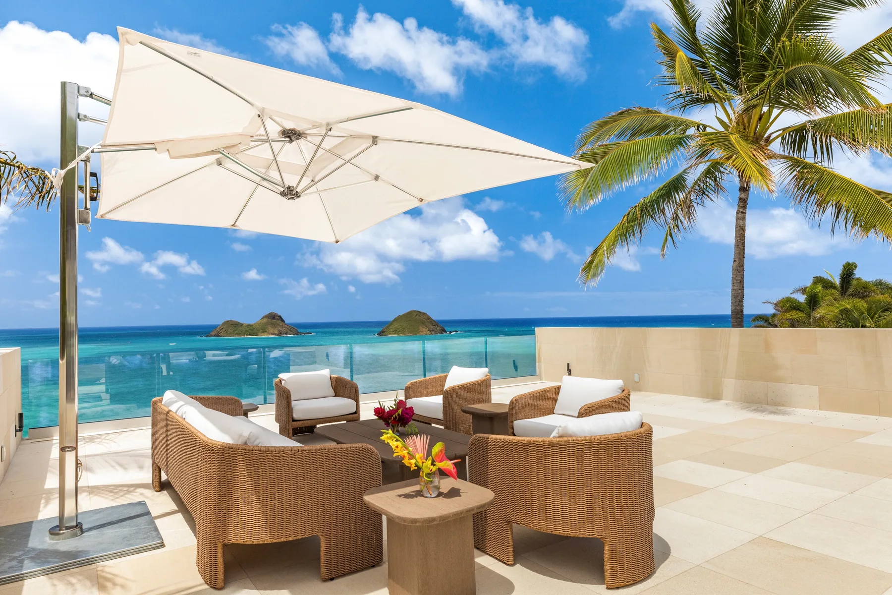 An outdoor patio with seating under a large umbrella overlooking the ocean.