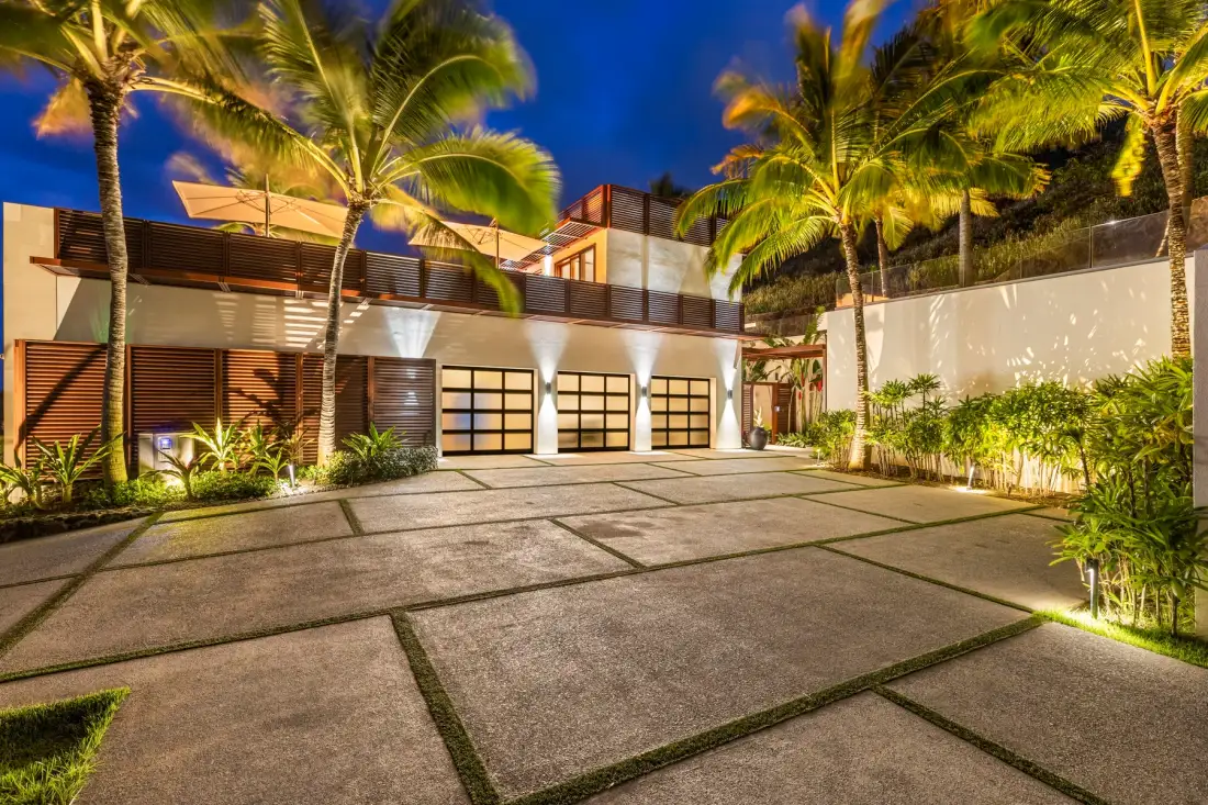 A modern building and paved courtyard are illuminated among palm trees at night.